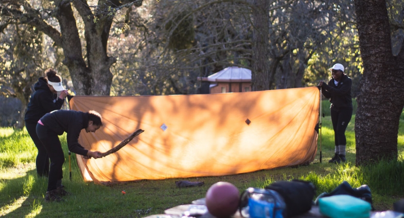 a group of people work together to set up a a tarp shelter on an outward bound course for bipoc